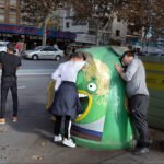Playful Recycling Bin Brings Joy to City Street Scene Playful recycling bin with graffiti face in busy urban street scene.