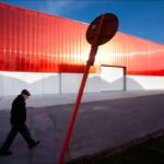 Elderly Man Walking Past Modern Red Building Elderly man walking past modern red building with stop sign at sunset.