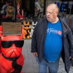 Whimsical Red Bulldog Statue in Vibrant Street Market Colorful red bulldog statue with sunglasses in lively street market scene.