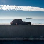Peaceful Ocean View With Person Resting on Ledge Person relaxing on concrete ledge overlooking ocean horizon with blue sky and island view.