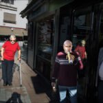 Man Eating Banana on Sunny European Street Scene Sunny European street scene with pedestrians, café shops, and man eating banana.