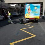 City Worker Sweeping Street Beside Delivery Truck Street worker sweeping near Amstel Radler delivery truck on busy urban city street.