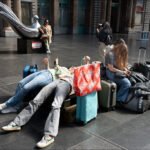 Travelers Resting with Luggage at Busy Train Station Tired travelers resting with luggage at busy train station.