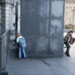 Girl Playing Hide and Seek with Street Musician Girl hiding near street musician playing accordion in urban square with stone architecture.