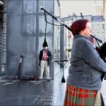 Bagpiper Performing on Rainy City Street Scene Bagpiper performing on rainy city street with modern architecture and pedestrians.