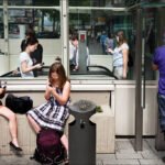 Girls on Smartphones Outside Busy City Transit Station Two young girls using smartphones outside busy urban transit station with commuters in background.