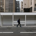 Solitary Man Walking Past Empty City Booths Man walking past empty white market booths in urban city street scene.