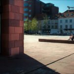 Modern City Plaza With Glass Architecture and People Relaxing Modern urban plaza with glass building, stone architecture, people relaxing, and sunny blue sky.
