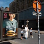 Religious Parade Passing Fast Food Burger Advertisement City parade with religious procession passing fast food burger advertisement in urban street scene.
