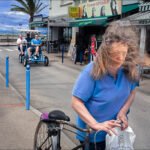 Lively Coastal Street With Bicycles, Shops, and Palm Trees Bustling coastal town street with woman, bicycle, tricycle riders, shops, and palm trees.
