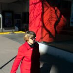 Woman in Red Coat Walking Through Sunlit City Street Woman in red coat walking on sunny city street with urban background.
