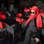 Woman in Red Hijab Walking by Outdoor Café Woman in red hijab walking past outdoor café with red chairs and modern urban style.