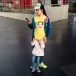 Mother and Child Sharing a Moment in Busy Mall Mother and child standing in busy shopping mall with phone and colorful clothing.