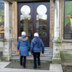Elderly Women Enter Ornate Building With Colorful Bird Art Elderly women walking to ornate historic building with colorful bird art on windows.