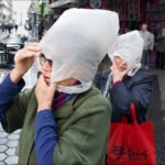 Elderly Women Use Plastic Bags as Rain Protection Elderly women cover heads with plastic bags while walking in rainy city street.
