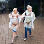 Women Walking in Playful Lingerie-Style Rain Ponchos Women walking in rain wearing transparent ponchos on a lively city street.