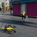 Father and Child Walking Past Yellow Bike in City Plaza Urban plaza with yellow bicycle, market stall, modern buildings, father and child walking.