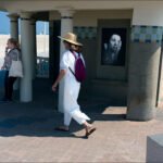 Women by seaside pavilion with art mural on sunny beach.