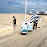 Relaxing beach scene with family, sandy shore, seaside bar, and overcast summer sky.