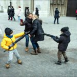 Children playing tug-of-war with umbrella in busy city square on a cold day.