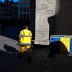 City maintenance worker cleaning cobblestone square near historic building entrance in daylight.