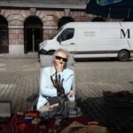 Elderly woman selling vintage jewelry at a bustling outdoor flea market.