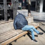 Headless person sitting on urban bench in city square under sunlight.