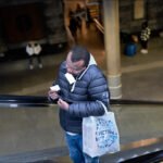 Man standing on escalator holding ticket in busy urban station.