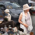 Woman browsing antique market table with vintage collectibles and porcelain bust.