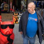 Vibrant red bulldog statue with sunglasses amusing shoppers at a colorful street market.