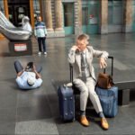 Business traveler and casual tourist in modern airport terminal with metallic bird sculpture.