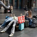 Travelers resting with colorful luggage in busy modern airport terminal.