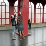 Playful urban couple with umbrella in modern train station setting.