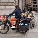 Father riding electric bike with three children on city street, family urban cycling adventure.