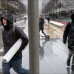 Two men walking through rainy city streets with reflections and urban hustle.