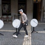 Man walking past outdoor café tables on cobblestone street near urban bar.