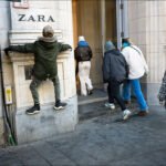 Young boy climbing wall outside Zara store on busy city shopping street.